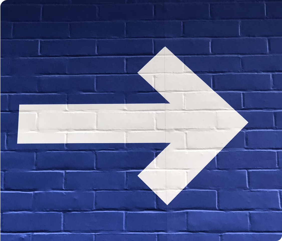 White arrow painted on a blue brick wall pointing to the right.